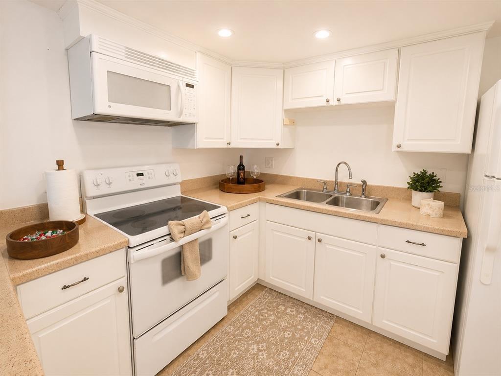 A kitchen featuring white cabinets, a white electric stove, and tan countertops — 5820 N CHURCH AVENUE UNIT 112, TAMPA, FL