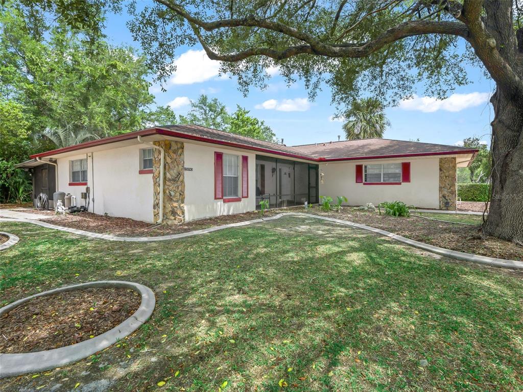 A single-story house with a screened porch, stone accents, and red shutters under large trees — 15090 SW 35TH CIRCLE, OCALA, FL