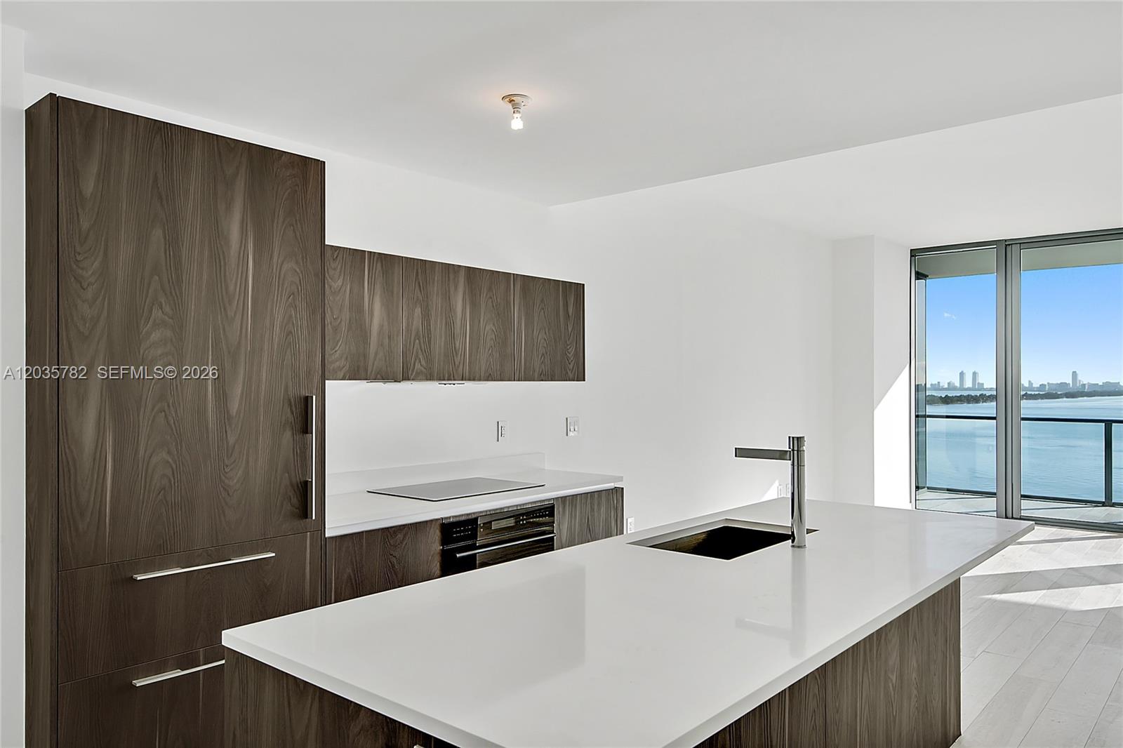 A modern kitchen features dark wood cabinetry, white countertops, a central island, and a balcony — 480 NE 31st St # 904, Miami FL 33137, MIAMI, FL