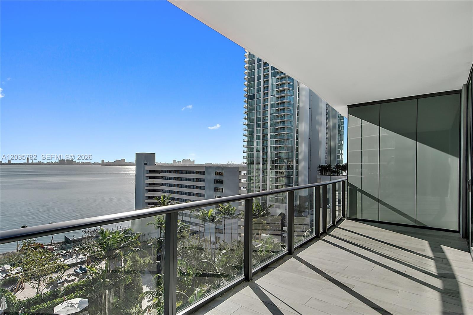 A high-rise balcony features gray tile flooring, a glass railing, and a waterfront city view — 480 NE 31st St # 904, Miami FL 33137, MIAMI, FL