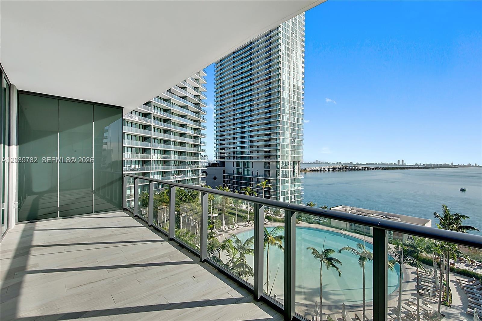 A balcony with tile flooring overlooks a swimming pool, high-rise buildings, and the ocean — 480 NE 31st St # 904, Miami FL 33137, MIAMI, FL