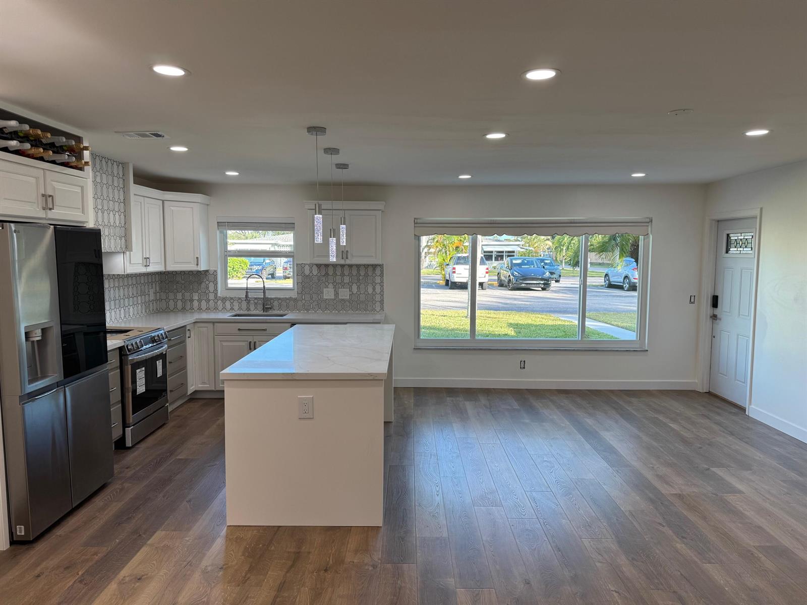 A modern kitchen features white cabinetry, a marble-topped island, and wood-look flooring — 917 S Drive Terrace # B, Delray Beach FL 33445, DELRAY BEACH, FL
