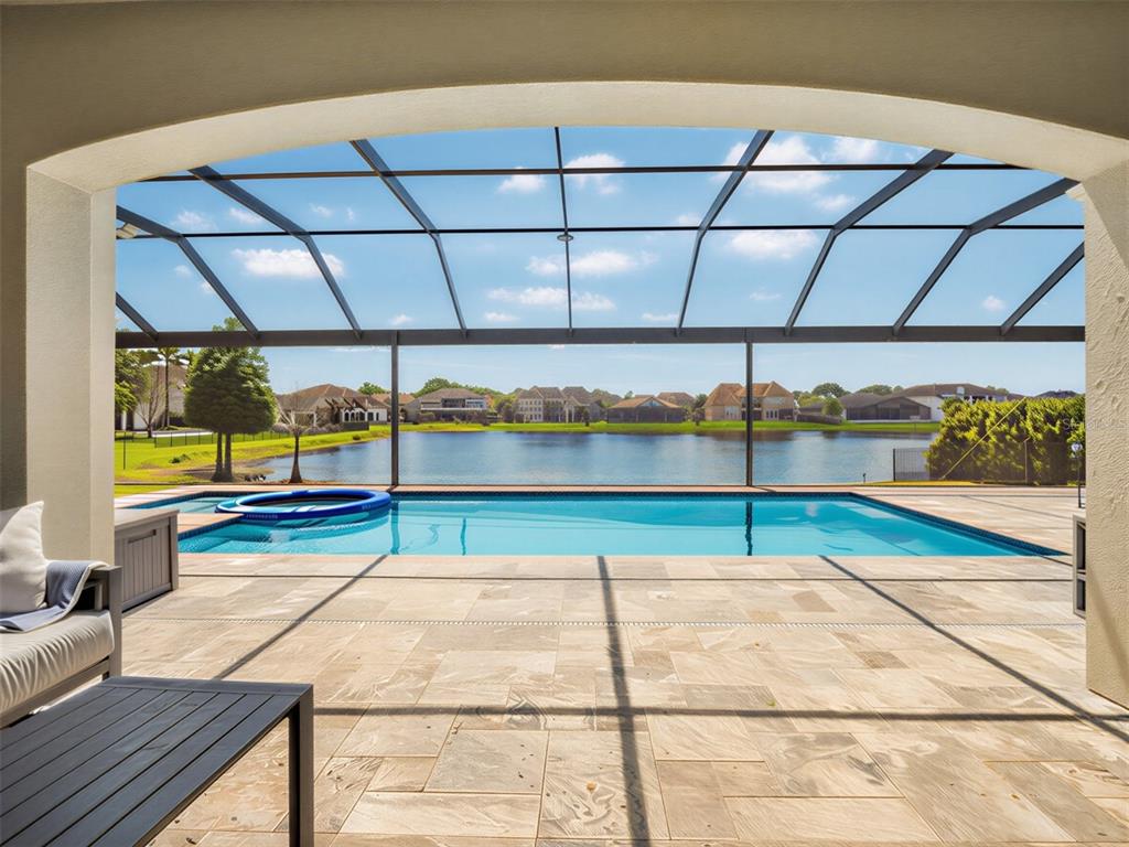 A covered patio overlooks a swimming pool and a lake surrounded by residential homes — 7654 BLUE QUAIL LANE, ORLANDO, FL