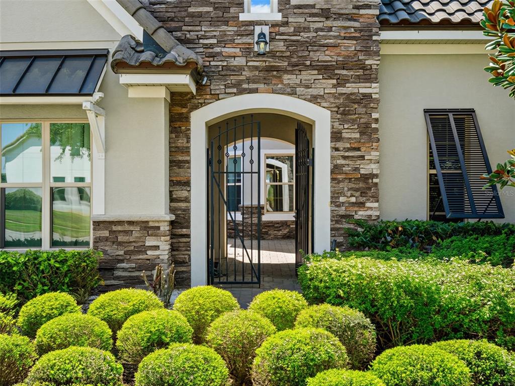 A stone-faced entryway features a black metal gate leading to a small courtyard — 7654 BLUE QUAIL LANE, ORLANDO, FL