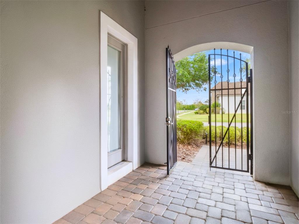 A paved entryway features a glass door and an open arched wrought iron gate — 7654 BLUE QUAIL LANE, ORLANDO, FL