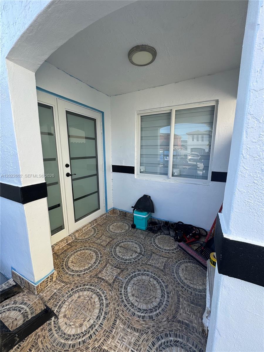 A covered entryway features a tiled floor with circular patterns, a glass door, and a window — 14017 SW 160th Ter, Miami FL 33177, MIAMI, FL