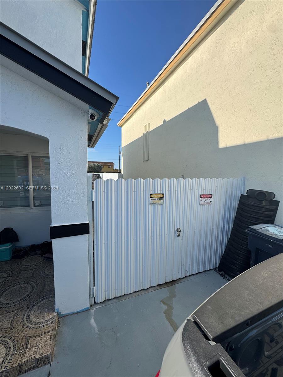 A white corrugated metal gate stands between two exterior walls of a residential building — 14017 SW 160th Ter, Miami FL 33177, MIAMI, FL