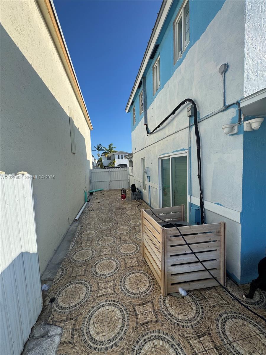 A narrow side yard features patterned tile flooring, a wooden AC enclosure, and a sliding door — 14017 SW 160th Ter, Miami FL 33177, MIAMI, FL