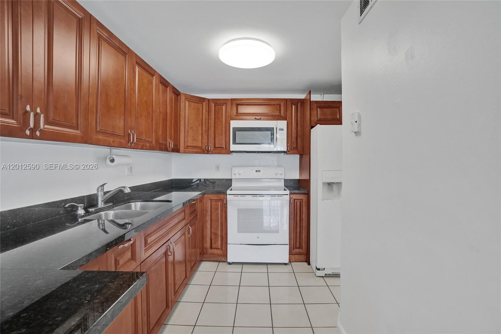A kitchen features wood cabinets, black granite countertops, white appliances, and light tile flooring — 14250 SW 62nd St # 408, Miami FL 33183, MIAMI, FL