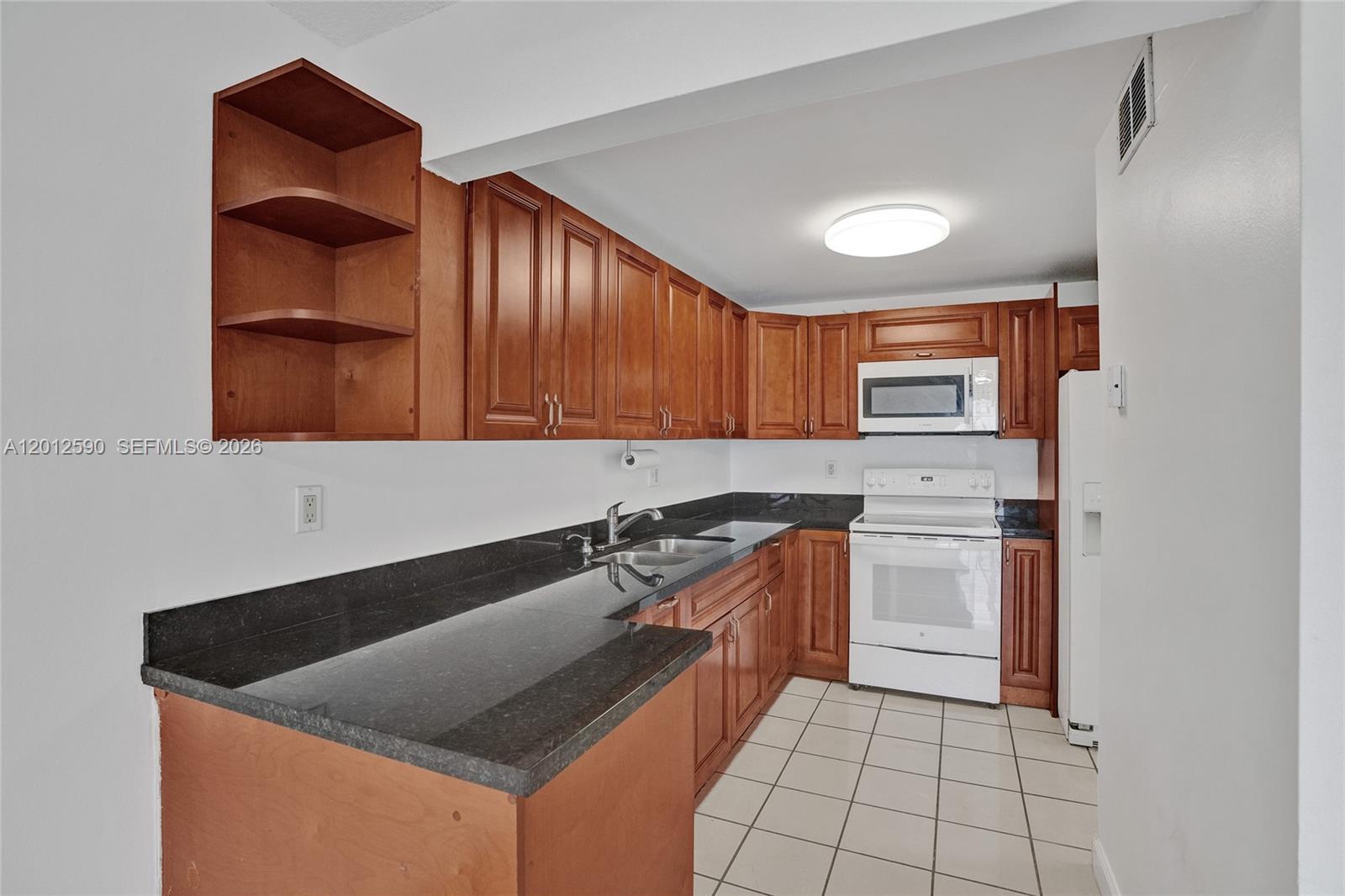 A kitchen features wood cabinets, black countertops, white appliances, and light-colored tile flooring — 14250 SW 62nd St # 408, Miami FL 33183, MIAMI, FL