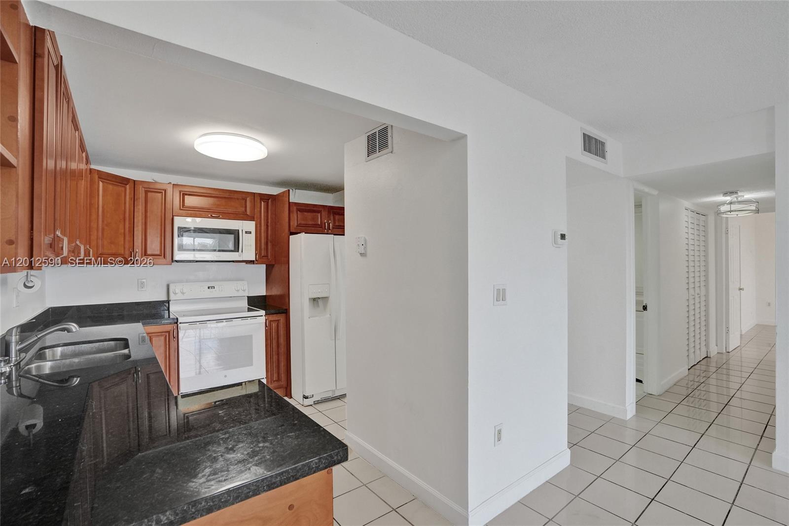 A kitchen features wood cabinets, black countertops, white appliances, and light-colored floor tiles — 14250 SW 62nd St # 408, Miami FL 33183, MIAMI, FL