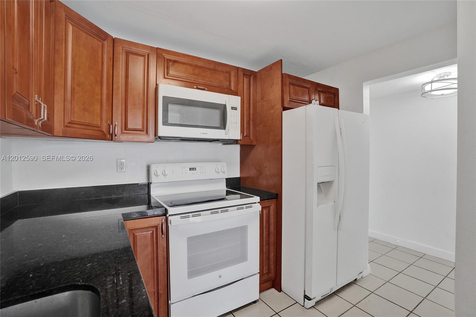A kitchen features wood cabinets, black countertops, and white appliances — 14250 SW 62nd St # 408, Miami FL 33183, MIAMI, FL