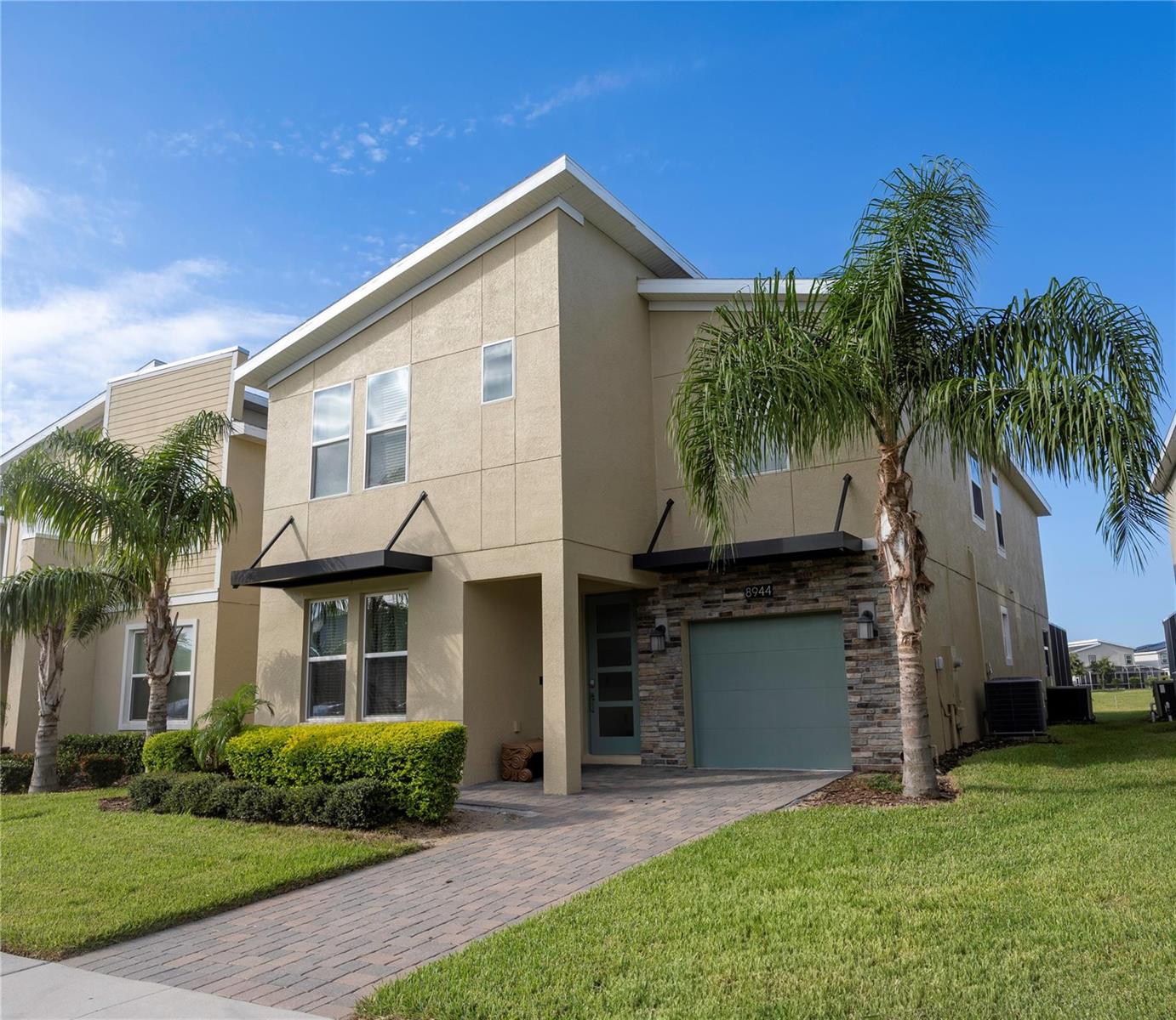 A two-story tan stucco house with a stone-accented garage and a palm tree in front — 8944 Cabot Cliffs Drive, Davenport FL 33896, DAVENPORT, FL