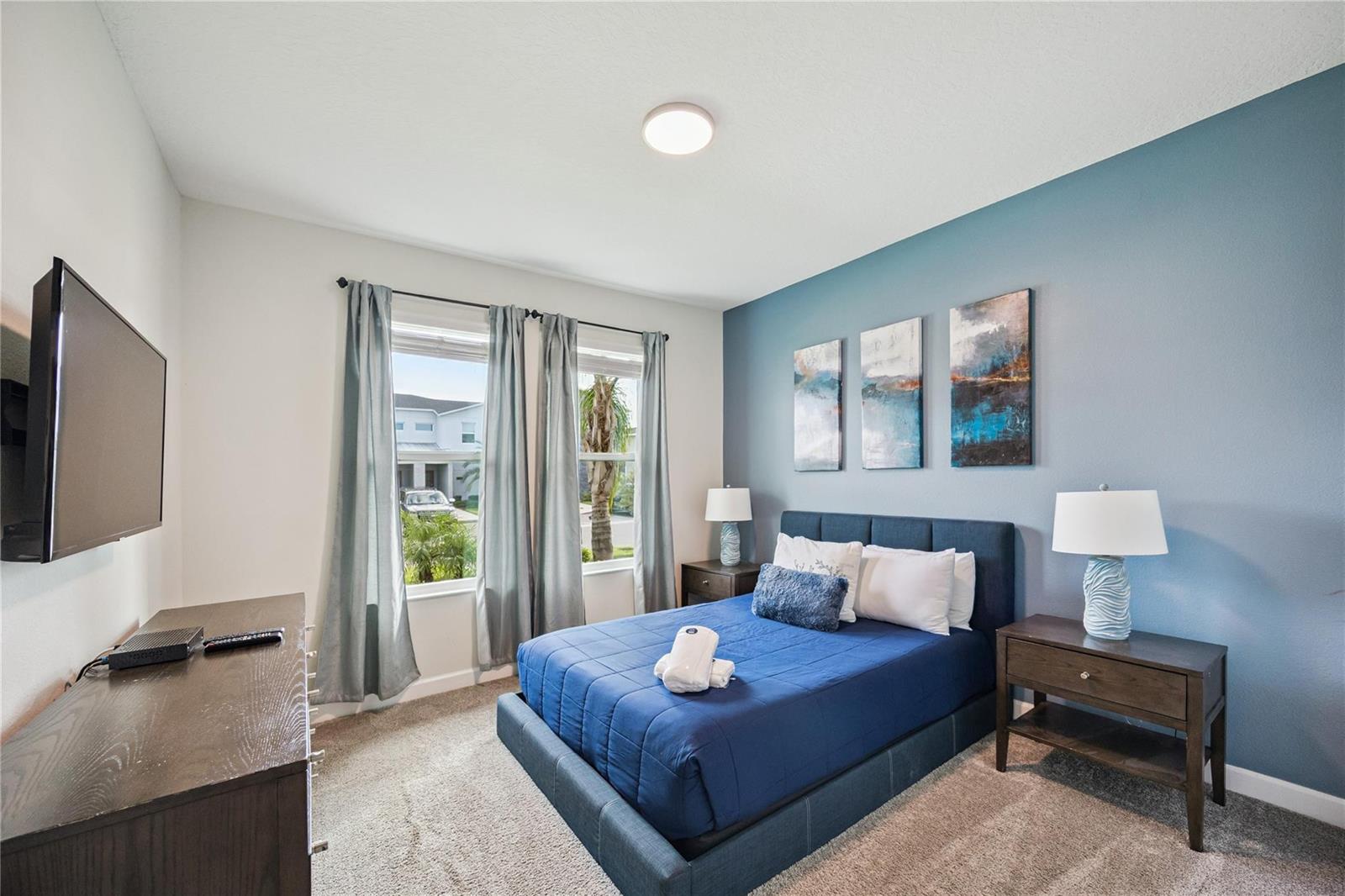 A bedroom features a blue accent wall, a bed with blue bedding, and two windows — 8944 Cabot Cliffs Drive, Davenport FL 33896, DAVENPORT, FL