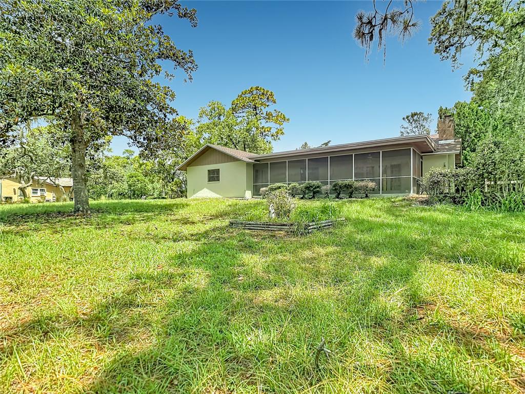 A single-story house with a screened-in porch sits on a grassy lot with trees — 10050 DEER LANE, NEW PORT RICHEY, FL