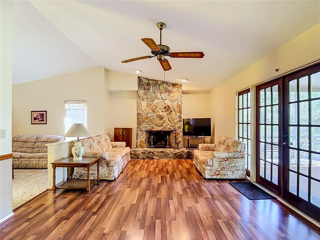 A living room features a stone fireplace, wood-look flooring, floral sofas, and glass patio doors — 10050 DEER LANE, NEW PORT RICHEY, FL