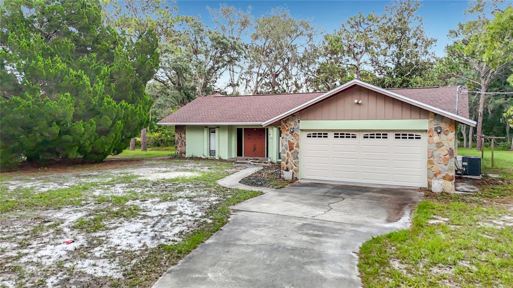 A single-story house with a stone facade, light green siding, and a two-car garage — 10050 DEER LANE, NEW PORT RICHEY, FL