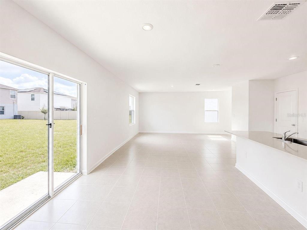 A bright, open-concept living area features light tile flooring, a sliding glass door, and windows — 2432 BLUESTONE ROAD, HAINES CITY, FL