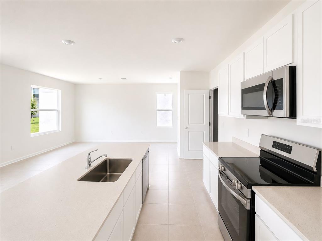 A modern kitchen with white cabinets, stainless steel appliances, and an island overlooks an area — 2432 BLUESTONE ROAD, HAINES CITY, FL
