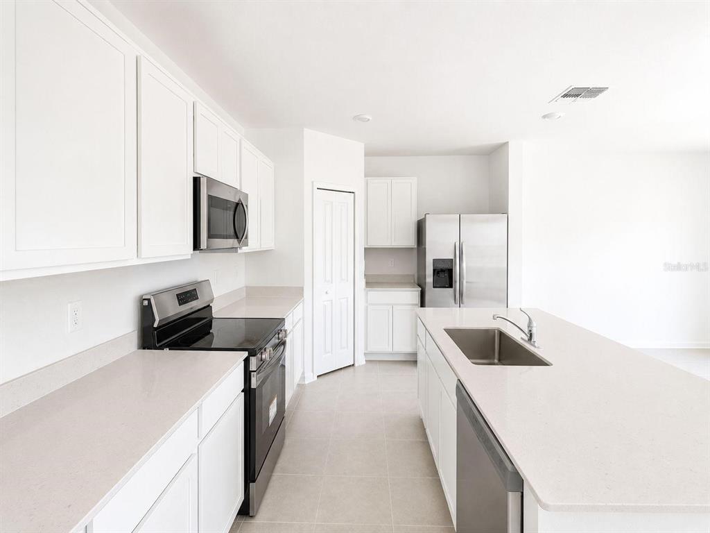 A modern kitchen features white cabinets, stainless steel appliances, and a large quartz island — 2432 BLUESTONE ROAD, HAINES CITY, FL