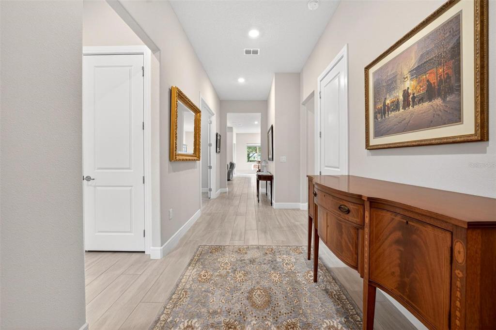 A hallway with light wood-look tile flooring, a wooden sideboard, and framed wall art — 9021 SW 57TH PLACE ROAD, OCALA, FL