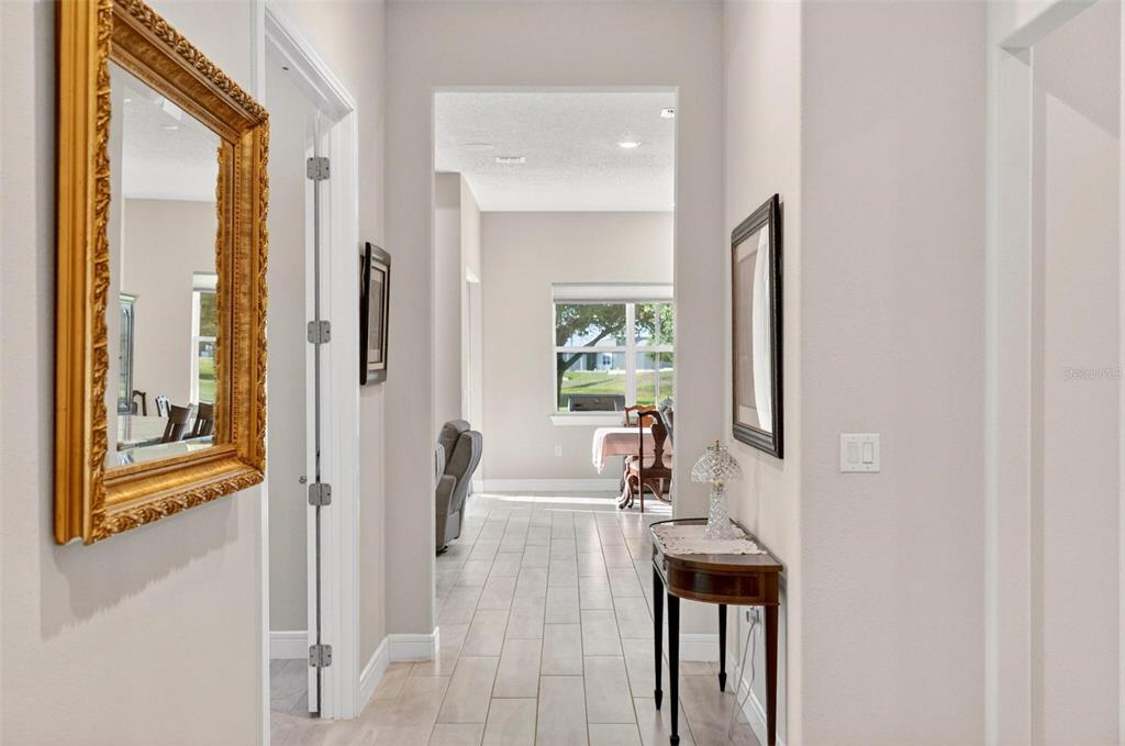 A hallway with light tile flooring leads to an open living area with a window — 9021 SW 57TH PLACE ROAD, OCALA, FL