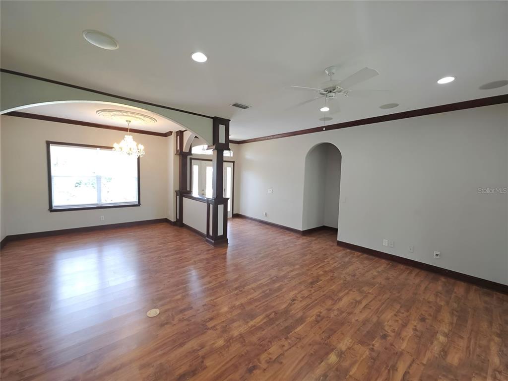 An empty living room features wood-look flooring, crown molding, a ceiling fan, and arched entryways — 3564 LASLO AVENUE, NORTH PORT, FL