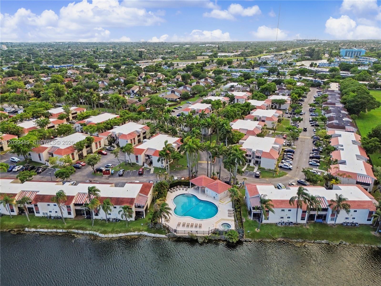 An aerial view shows a residential complex with a swimming pool beside a lake — 3rd Ct 20135 # 1, Miami FL 33179, MIAMI, FL