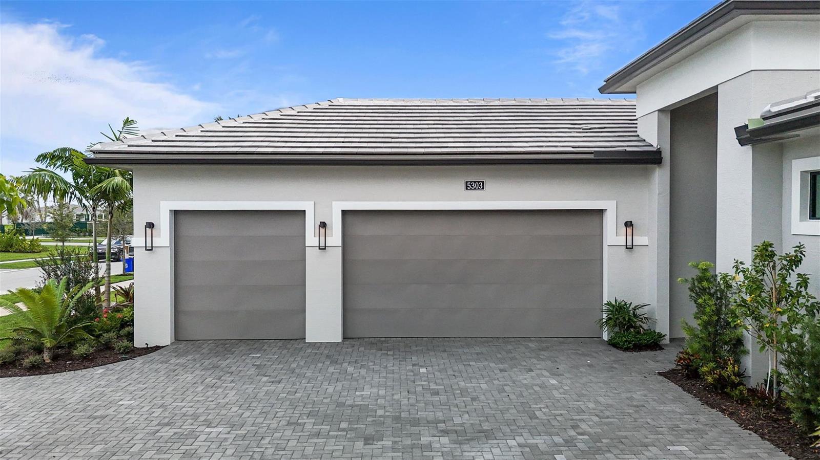 A gray house exterior features a three-car garage with paved driveway and landscaping — 5303 Saint Armands Way, Westlake FL 33470, WESTLAKE, FL