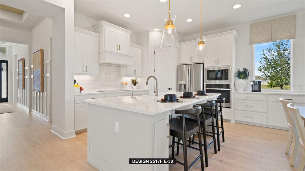 A modern white kitchen features a large center island, stainless steel appliances, and pendant lighting — 3904 COUNTRY VIEW COURT, BRADENTON, FL