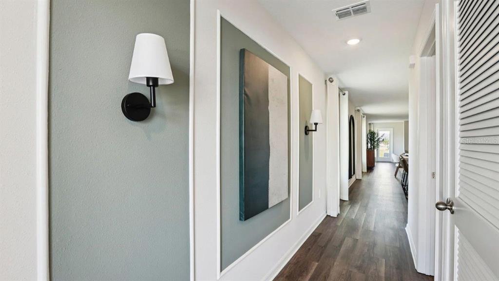 A hallway features sage green wall panels, white sconces, and wood-look flooring — 3010 VICEROY COURT, POINCIANA, FL