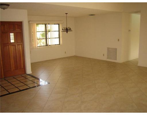 An empty room with light-colored tile flooring, a wooden front door, and a hanging chandelier — 6050 Amberwoods Drive, Boca Raton FL 33433, BOCA RATON, FL