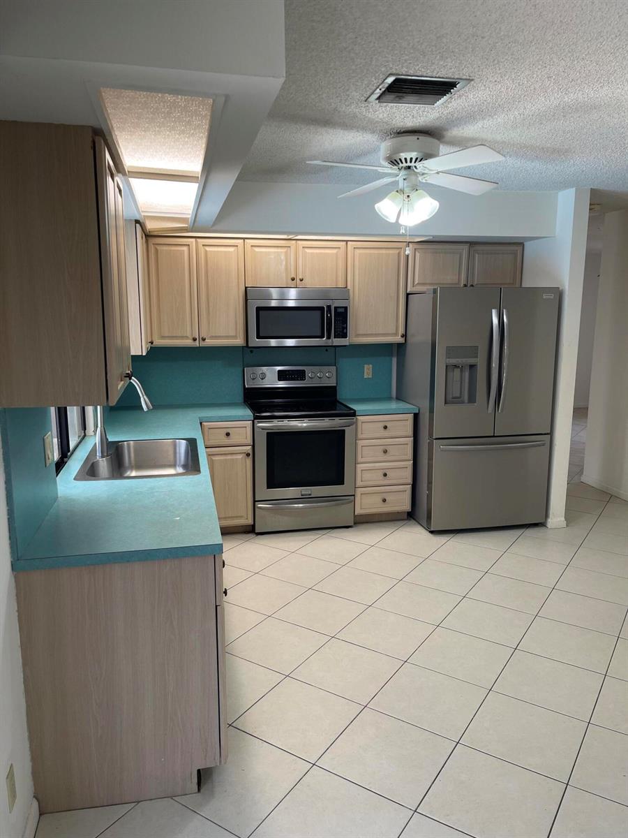 A kitchen features light wood cabinets, teal countertops, stainless steel appliances, and tiled flooring — 6050 Amberwoods Drive, Boca Raton FL 33433, BOCA RATON, FL