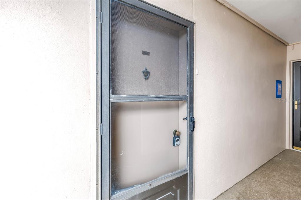 A metal screen door with a lockbox is mounted on a beige exterior wall — 7700 SUN ISLAND DRIVE S UNIT 402, SOUTH PASADENA, FL