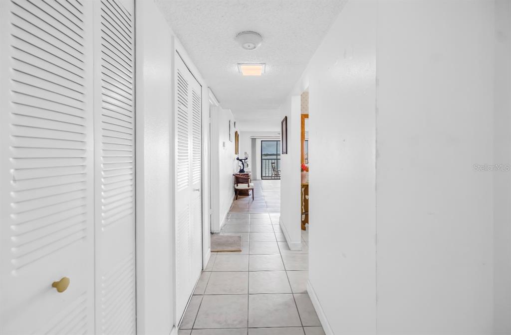 A white hallway with tiled floors leads toward a balcony with a water view — 7700 SUN ISLAND DRIVE S UNIT 402, SOUTH PASADENA, FL