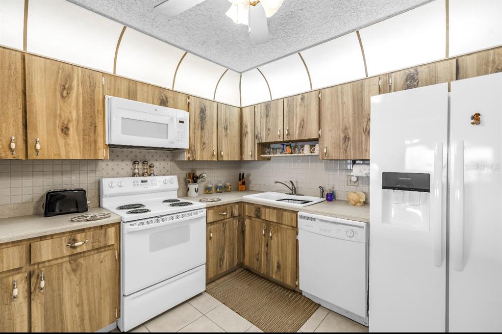 A kitchen features wood-grain cabinets, white appliances, a tiled backsplash, and a white sink — 7700 SUN ISLAND DRIVE S UNIT 402, SOUTH PASADENA, FL
