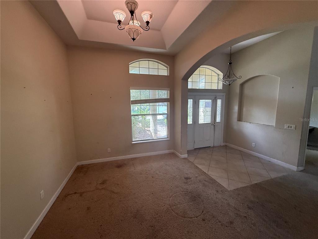 A carpeted living room features a tray ceiling, a chandelier, and an arched entryway — 1920 ELOISE COVE DRIVE, WINTER HAVEN, FL