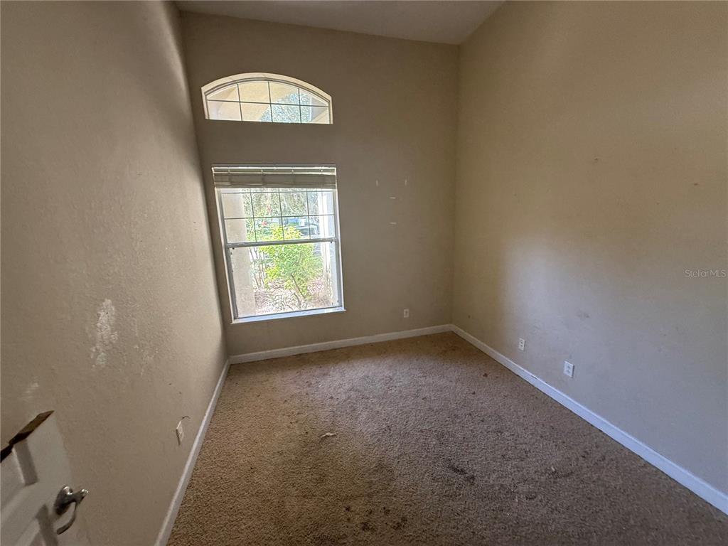An empty bedroom features beige carpet, tan walls, a window with blinds, and an arched transom — 1920 ELOISE COVE DRIVE, WINTER HAVEN, FL