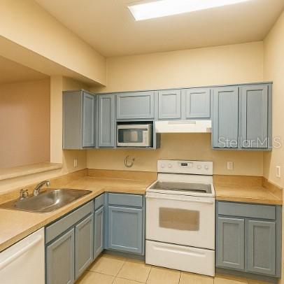 A kitchen with light blue cabinets, a white stove, a microwave, and tan countertops — 3701 CASTLE PINES LANE UNIT 3914, ORLANDO, FL
