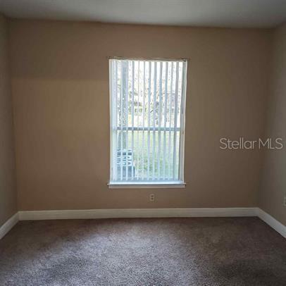 A bedroom with beige walls, brown carpet, and a window covered by vertical blinds — 3701 CASTLE PINES LANE UNIT 3914, ORLANDO, FL