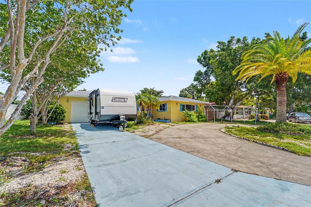 A yellow house with a driveway, a parked travel trailer, and a large palm tree — 9735 50TH AVENUE N, MADEIRA BEACH, FL