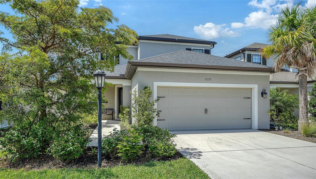 A two-story house features a light gray exterior, a two-car garage, and a landscaped yard — 8278 VELDA TRAIL, SARASOTA, FL
