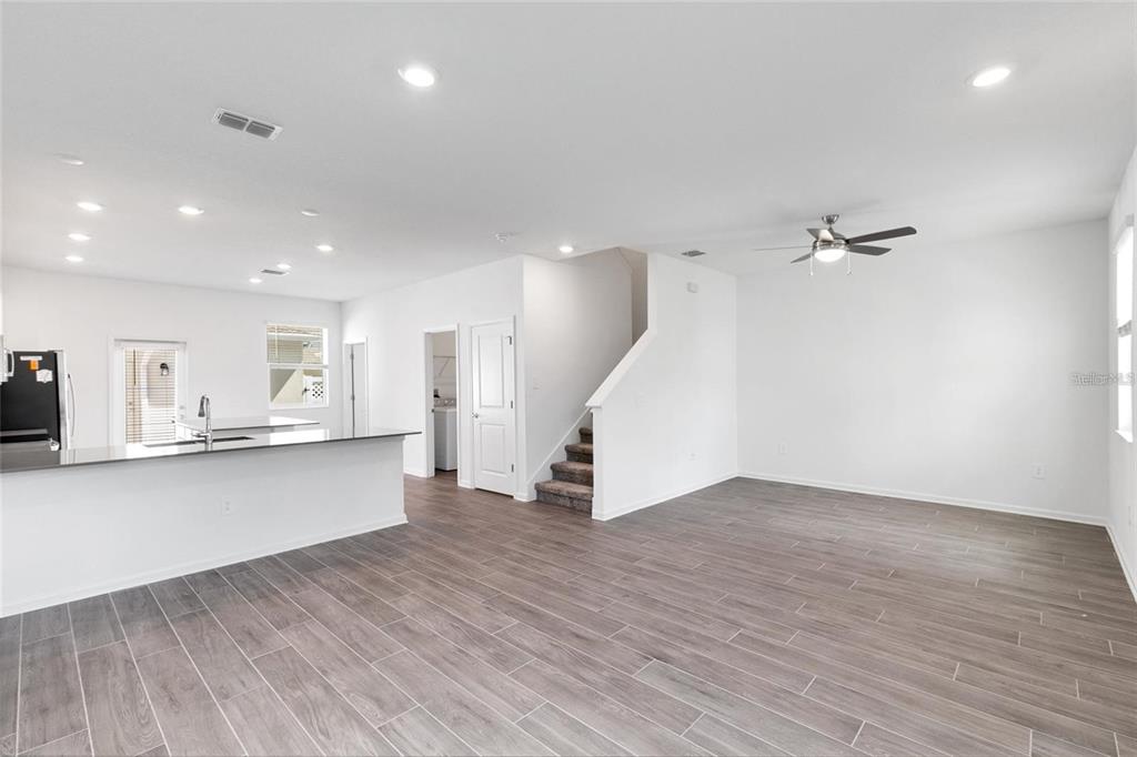 An open-concept living area features wood-look tile flooring, a kitchen island, and a staircase — 10540 TRIBUTE DRIVE, WINTER GARDEN, FL