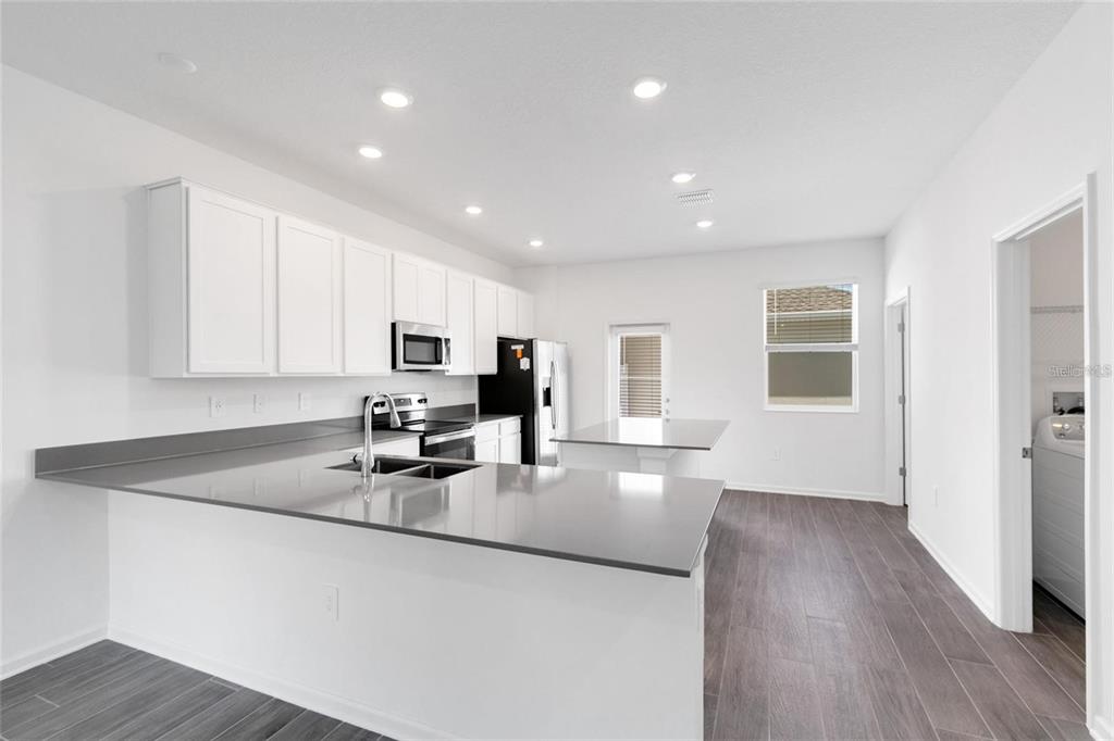 A modern kitchen features white cabinets, gray countertops, and dark wood-look flooring — 10540 TRIBUTE DRIVE, WINTER GARDEN, FL