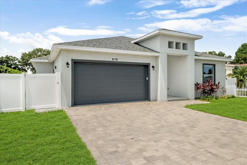 A single-story house exterior features a gray two-car garage, white stucco walls, and paver driveway — 6175 109TH AVENUE N, PINELLAS PARK, FL