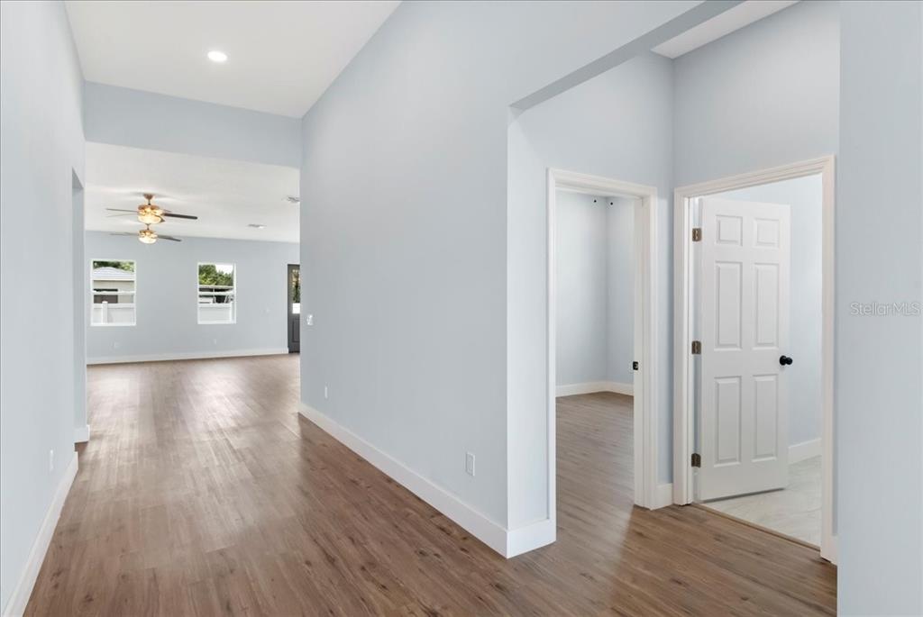 A hallway with light blue walls and wood-look flooring leads to an open living area — 6175 109TH AVENUE N, PINELLAS PARK, FL
