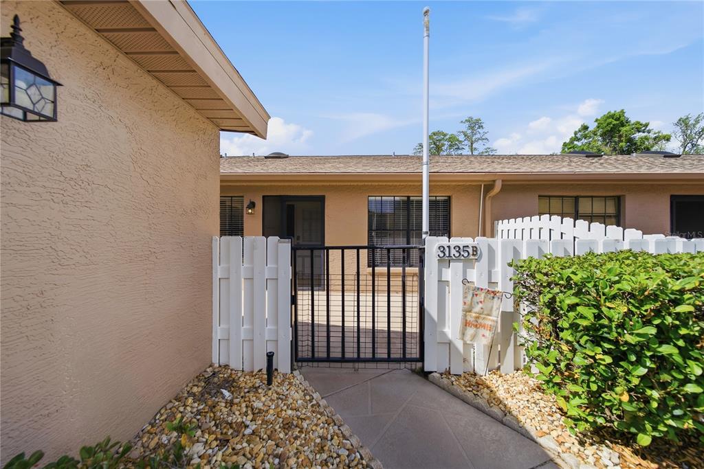 A gated walkway leads to the entrance of a single-story home with a tan exterior — 3135 CHARTER CLUB DRIVE UNIT B, TARPON SPRINGS, FL