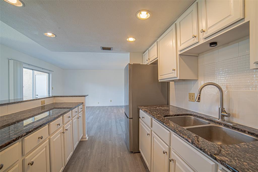 A kitchen with white cabinets, dark granite countertops, and stainless steel appliances opens to living — 629 N KEENE ROAD UNIT T11, CLEARWATER, FL