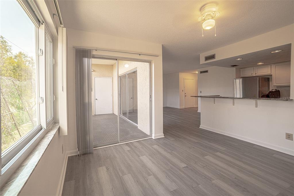 A living area with gray wood-look flooring, a sliding glass door, and an open kitchen — 629 N KEENE ROAD UNIT T11, CLEARWATER, FL