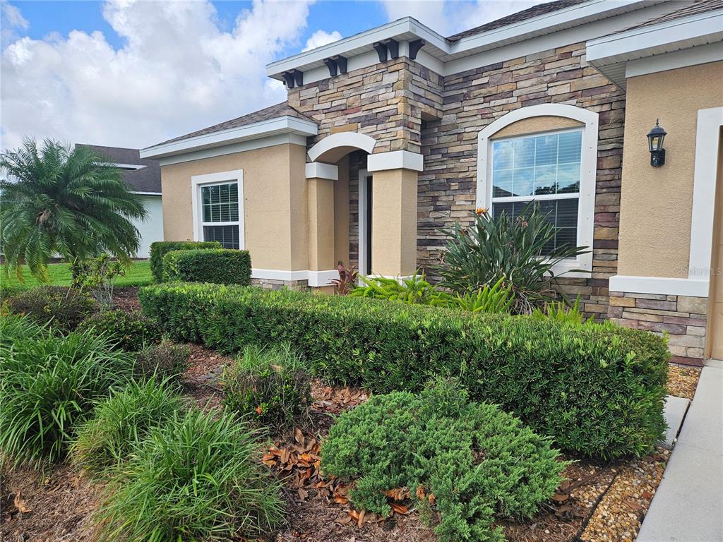 A single-story house exterior features tan stucco walls, stone veneer accents, and manicured landscaping — 924 BUTTERCUP GLEN, BRADENTON, FL
